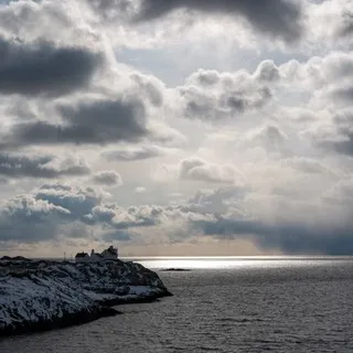 The lighthouse in Henningsvær, Stormy weather in the background with shimmers of sunshine